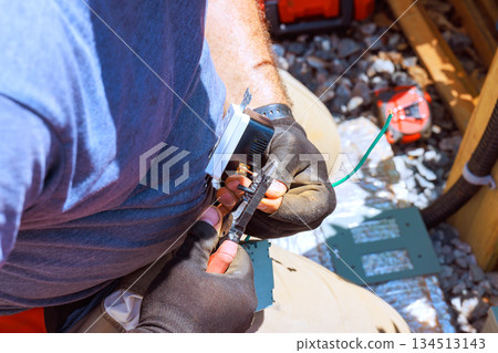 Worker fixes electrical wiring while sitting on wooden deck at construction site Worker fixes electrical wiring while sitting on wooden deck at construction site 134513143