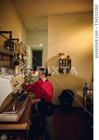 Hispanic middle-aged woman in a red sweater works behind a busy espresso bar in a warm, inviting cafe, highlighting hospitality and small business life. Hispanic middle-aged woman in a red sweater works behind a busy espresso bar in a warm, inviting cafe, highlighting hospitality and small business life. 134513168