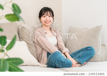 在家客廳的沙發上放鬆的微笑年輕亞洲女性 在家客廳的沙發上放鬆的微笑年輕亞洲女性 134513403