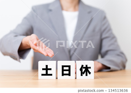 A middle-aged female business woman wearing a suit and a block of weekends off A middle-aged female business woman wearing a suit and a block of weekends off 134513636