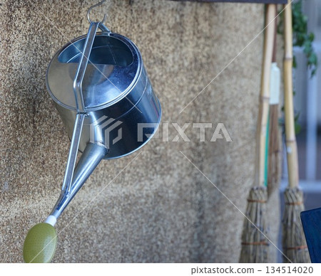A silver watering can and broom mounted on the wall 134514020