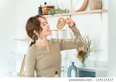 一位時尚的亞洲女性在廚房裡吃麵包。 134514337