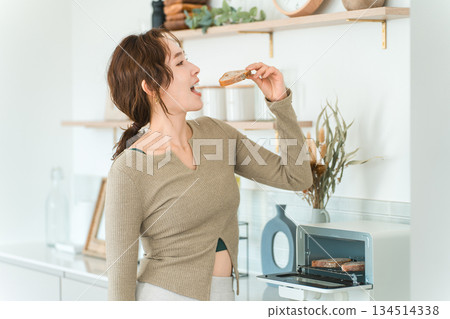 Stylish Asian woman eating bread in the kitchen 134514338