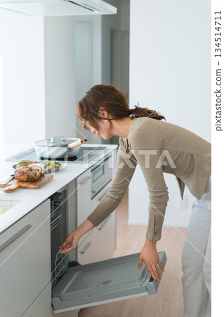 A young Asian woman using a dishwasher in a system kitchen A young Asian woman using a dishwasher in a system kitchen 134514711