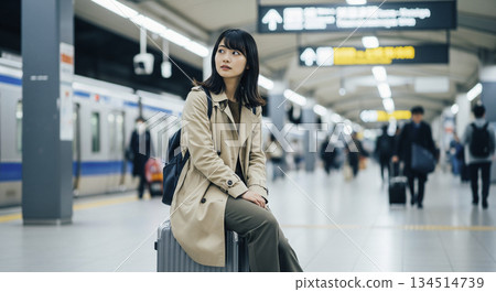 一位女士坐在行李箱上等火車。 134514739