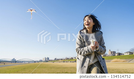 A woman flying a kite on the riverbank 134514752