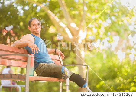 Venezuelan athlete with prosthetic legs resting on park bench smiling to camera 134515268