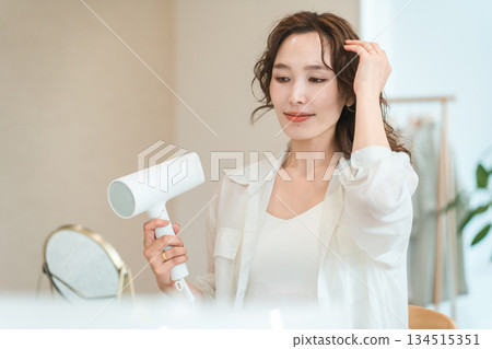 A woman blow-drying her hair with a hair dryer (hair care) 134515351