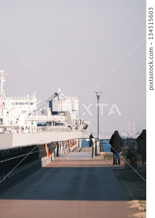 A winter pier promenade with a huge ship passing by A winter pier promenade with a huge ship passing by 134515603