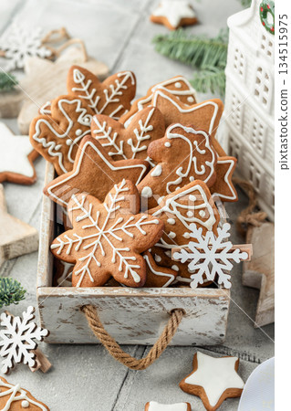 Christmas gingerbread cookies decorated with white icing in rustic wooden box. Festive holiday treats with pine branches and Christmas decor on white table Christmas gingerbread cookies decorated with white icing in rustic wooden box. Festive holiday treats with pine branches and Christmas decor on white table 134515975
