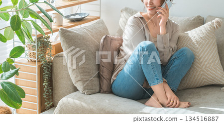 A stylish woman sitting on a sofa and talking on a smartphone A stylish woman sitting on a sofa and talking on a smartphone 134516887