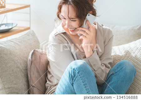 A stylish woman sitting on a sofa and talking on a smartphone A stylish woman sitting on a sofa and talking on a smartphone 134516888