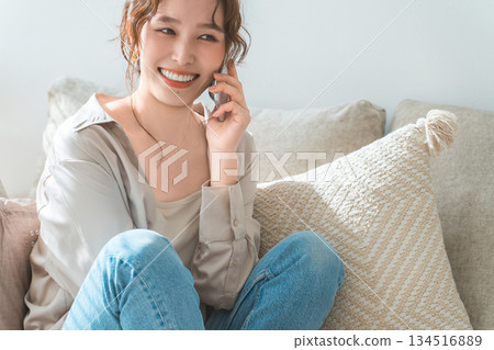 A stylish woman sitting on a sofa and talking on a smartphone A stylish woman sitting on a sofa and talking on a smartphone 134516889