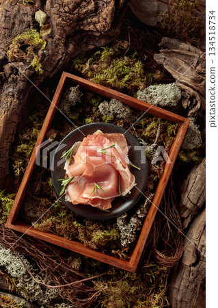 Prosciutto with rosemary on a black plate in abstract natural composition. 134518734