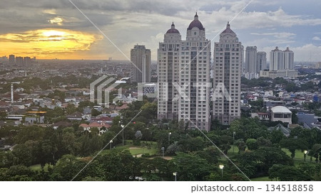 A glowing golf course with sand bunkers and floodlights stretches beneath ornate towers and a vivid sunset, blending sport, architecture, and nature in a dramatic dusk cityscape in Jakarta A glowing golf course with sand bunkers and floodlights stretches beneath ornate towers and a vivid sunset, blending sport, architecture, and nature in a dramatic dusk cityscape in Jakarta 134518858
