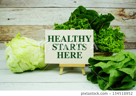 "Healthy Starts Here" message on a small easel next to a basket of fresh green leafy vegetables "Healthy Starts Here" message on a small easel next to a basket of fresh green leafy vegetables 134518952