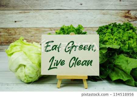 "Eat Green, Live Clean" message on a small easel next to a basket of fresh green leafy vegetables "Eat Green, Live Clean" message on a small easel next to a basket of fresh green leafy vegetables 134518956