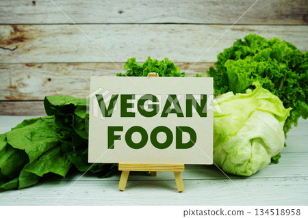 "Vegan Food" message on a small easel next to a basket of fresh green leafy vegetables "Vegan Food" message on a small easel next to a basket of fresh green leafy vegetables 134518958