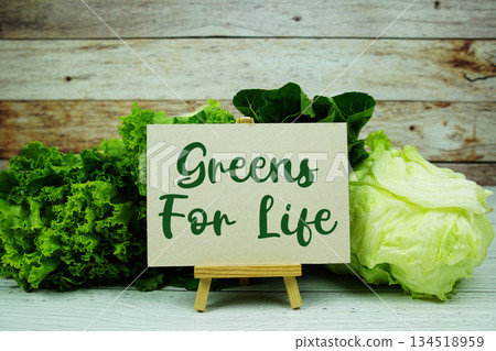 "Greens For Life" message on a small easel next to a basket of fresh green leafy vegetables "Greens For Life" message on a small easel next to a basket of fresh green leafy vegetables 134518959