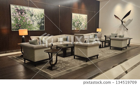 An elegant lounge with beige armchairs, floral rugs, and warm lighting offers a refined, tranquil space enriched by art, symmetry, and a metallic dragonfly sculpture casting a graceful shadow An elegant lounge with beige armchairs, floral rugs, and warm lighting offers a refined, tranquil space enriched by art, symmetry, and a metallic dragonfly sculpture casting a graceful shadow 134519709