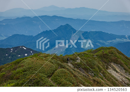 Climbers heading towards Yomogo Pass and the mountain range towards Echigo Yuzawa seen from Mount Takeno in the Tanigawa Mountain Range Climbers heading towards Yomogo Pass and the mountain range towards Echigo Yuzawa seen from Mount Takeno in the Tanigawa Mountain Range 134520563