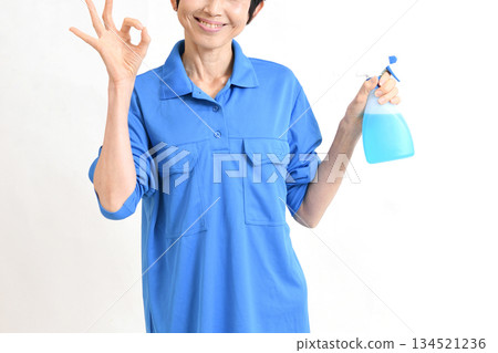 一位身穿工作服的中年亞裔女性，手持清潔噴霧，並比劃著「OK」手勢。 134521236