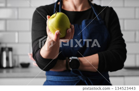 Girl In Apron Showing Raw Green Apple In Kitchen 134523443