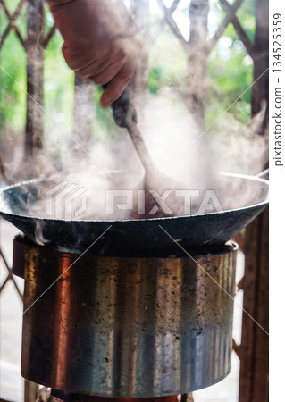 Hand stir frying in hot pan with smoky from traditional stove 134525359