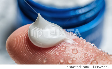 Close-up of white moisturizing cream being gently applied to a fingertip with fresh droplets of water Close-up of white moisturizing cream being gently applied to a fingertip with fresh droplets of water 134525439