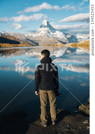 Man standing with camera at Lake Stellisee with Matterhorn mountain in Switzerland Man standing with camera at Lake Stellisee with Matterhorn mountain in Switzerland 134525453