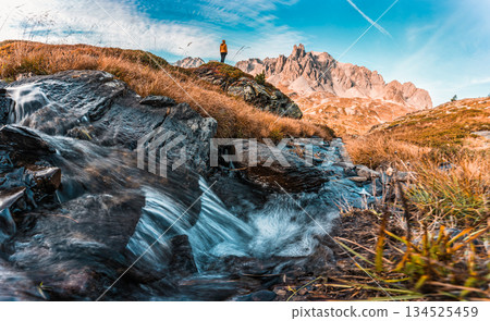 Landscape of female hiker standing on mountain with Massif Des Cerces, Main De Crepin peak and stream flowing in Claree Valley 134525459