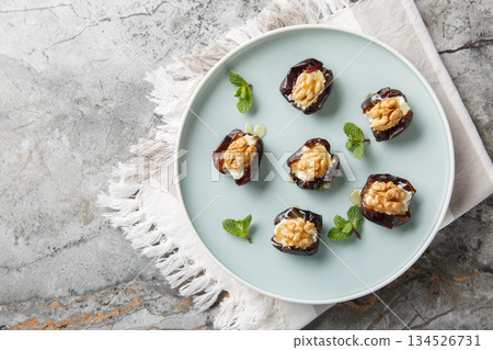 Sweet stuffed dates with cream cheese, walnuts and honey close-up in a plate. Horizontal top view 134526731
