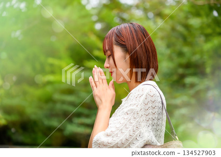 A woman quietly praying with her hands together against a background of fresh greenery A woman quietly praying with her hands together against a background of fresh greenery 134527903