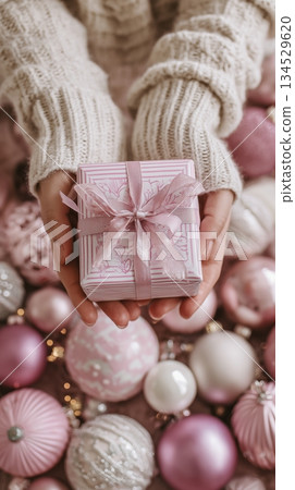 Gift Box Held Above Pink Holiday Decorations With Ornaments and Flowers 134529620