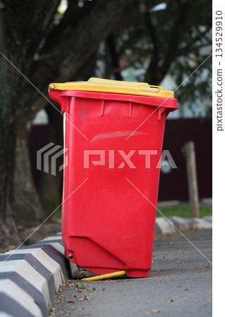 Red outdoor trash bin with a yellow lid placed on a roadside curb in an urban environment Red outdoor trash bin with a yellow lid placed on a roadside curb in an urban environment 134529910