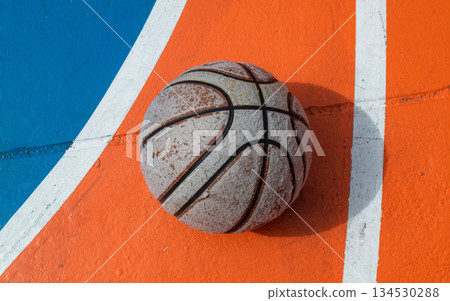 A worn, greyed basketball rests on the orange court, its long shadow a silent sentinel of countless games. A worn, greyed basketball rests on the orange court, its long shadow a silent sentinel of countless games. 134530288