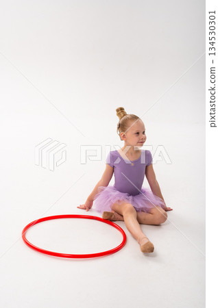 Child ballerina with cochlear implant sitting near red hoop. Inclusive beauty, hearing technology, and self-confidence expressed through dance and childhood joy. 134530301
