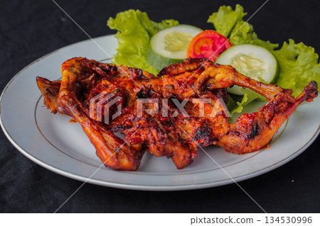 Spicy Ayam Taliwang, traditional grilled chicken dish from Lombok, Indonesia, served on a plate with fresh vegetables. Spicy Ayam Taliwang, traditional grilled chicken dish from Lombok, Indonesia, served on a plate with fresh vegetables. 134530996