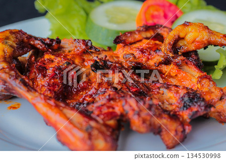Spicy Indonesian grilled chicken Ayam Bakar Taliwang served close-up on plate with fresh vegetable garnish Spicy Indonesian grilled chicken Ayam Bakar Taliwang served close-up on plate with fresh vegetable garnish 134530998