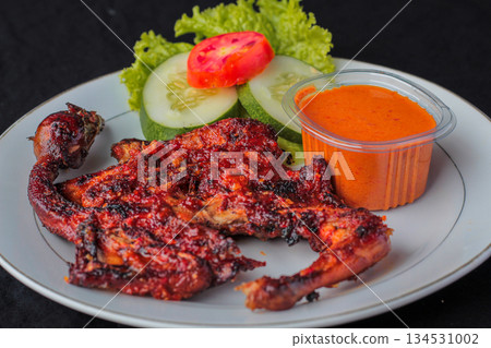 Ayam Taliwang, traditional Lombok spicy grilled chicken dish served on a plate with fresh vegetables and sambal chili sauce. Ayam Taliwang, traditional Lombok spicy grilled chicken dish served on a plate with fresh vegetables and sambal chili sauce. 134531002