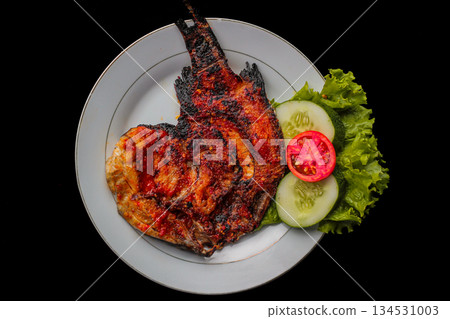 Grilled fish dish, spicy sambal sauce, Ikan Bakar, white plate, black background, Indonesian cuisine. Grilled fish dish, spicy sambal sauce, Ikan Bakar, white plate, black background, Indonesian cuisine. 134531003