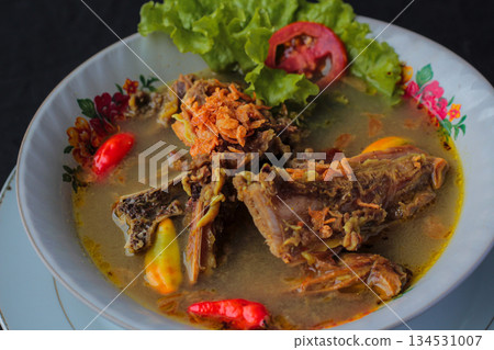 Indonesian traditional Sop Tulang served with fried shallots, chili, and lettuce on floral bowl. 134531007