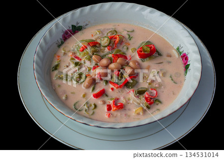Traditional Lombok vegetable coconut milk stew, Sayur Kacang Santan, served in white floral ceramic bowl against black background. 134531014