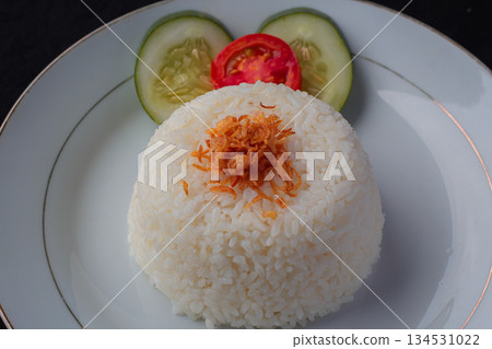 White rice portion topped with fried shallots and vegetable garnish on a simple plate. White rice portion topped with fried shallots and vegetable garnish on a simple plate. 134531022