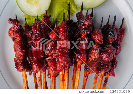 Sate Rembiga, traditional spicy grilled beef skewers from Lombok, Indonesia, served on a white plate with fresh cucumber. 134531029