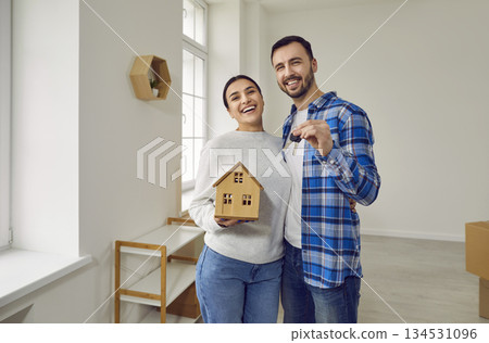 Happy married couple together hold keys to their new modern apartment and mock-up of toy house. Happy married couple together hold keys to their new modern apartment and mock-up of toy house. 134531096