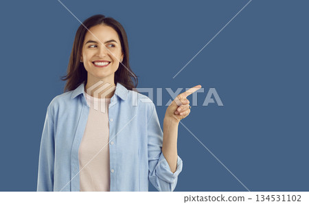 Happy young woman smiling and pointing her finger at copy space side on blue background Happy young woman smiling and pointing her finger at copy space side on blue background 134531102