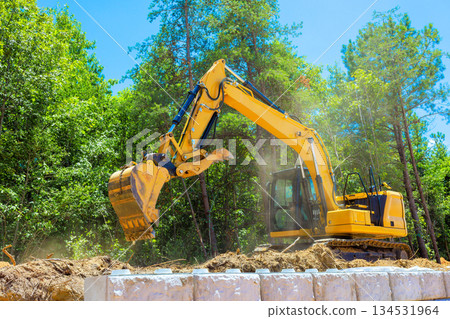 Large excavator is working to dig soil in forested area under construction site 134531964