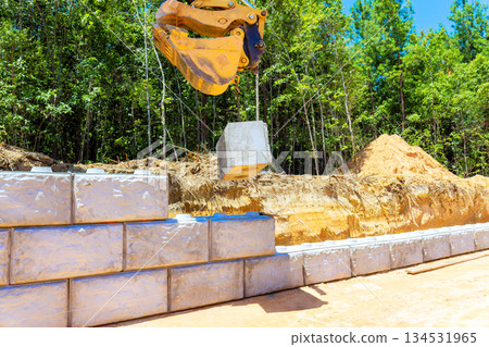 Heavy machinery lifts concrete block to place it on wall under creating retaining wall 134531965
