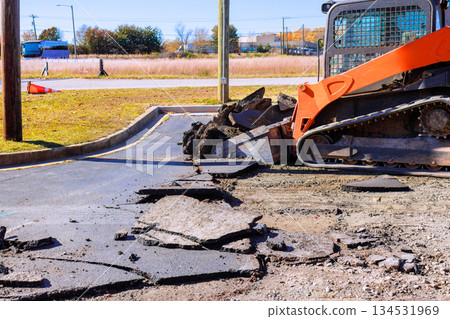 Machinery skid steer tears up old asphalt in parking lot, clearing space for upcoming reconstruction 134531969